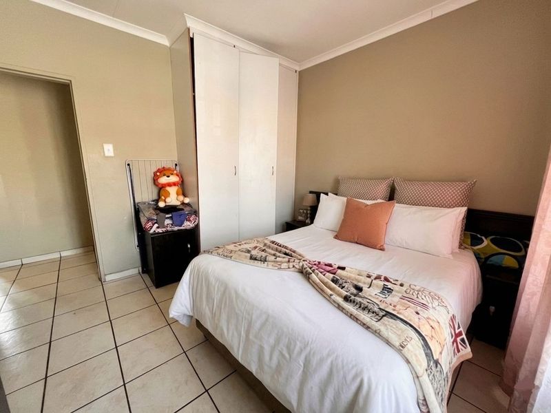 A functional bedroom featuring tiled flooring, neutral wall tones, and a built-in wardrobe for storage.