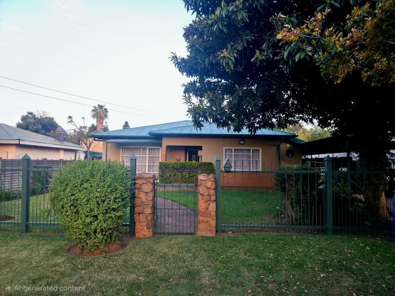Front view of a single-story house featuring a metal roof, stone-clad gate pillars, and a well-maintained front garden with perimeter fencing.