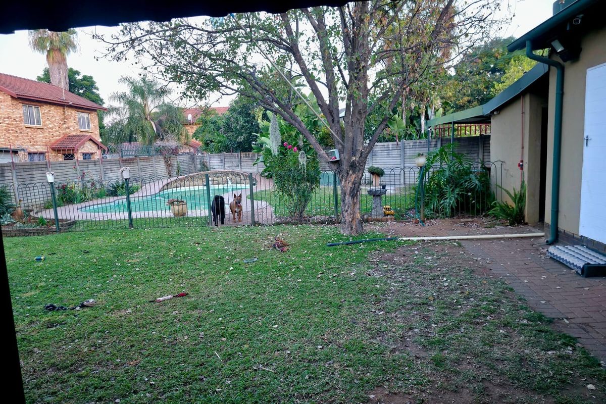 A rear garden view featuring a swimming pool, paved walkway, and perimeter wall, providing a functional outdoor space for the property.