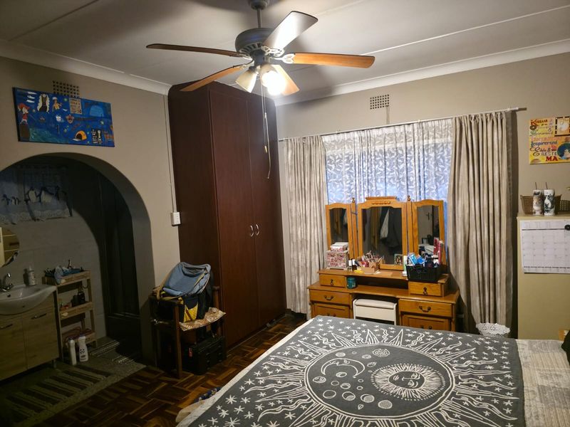 Bedroom featuring parquet flooring, a ceiling fan, built-in wardrobe, and an adjoining alcove with a wall-mounted basin.
