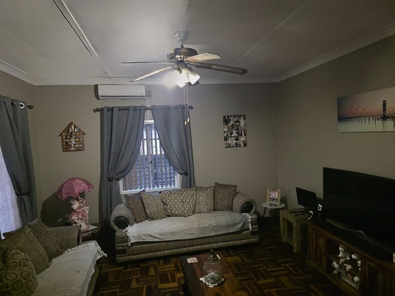 A cozy living room featuring classic parquet flooring, a ceiling fan, and a wall-mounted split-system air conditioner for climate control.