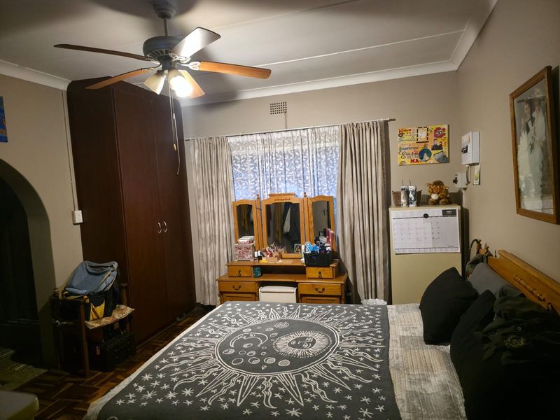 A bedroom featuring parquet flooring, a ceiling fan, and a built-in wardrobe, offering a functional space with traditional finishes.