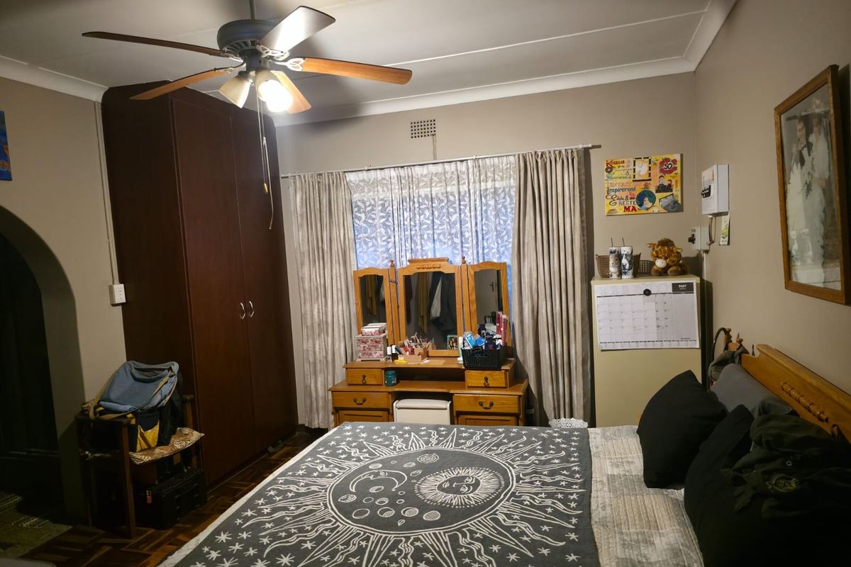 A bedroom featuring parquet flooring, a ceiling fan, and a built-in wardrobe, offering a functional space with traditional finishes.