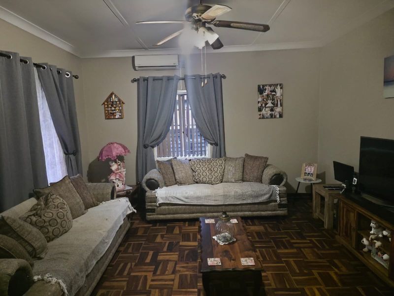 A comfortable living room featuring classic parquet flooring, a ceiling fan, and a wall-mounted split-system air conditioner.