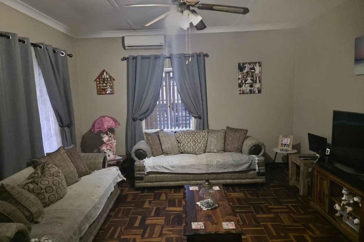 A comfortable living room featuring classic parquet flooring, a ceiling fan, and a wall-mounted split-system air conditioner.