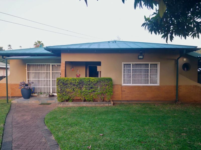 Front elevation of a single-story house featuring a metal roof, brick base, paved walkway, and a well-maintained front lawn.