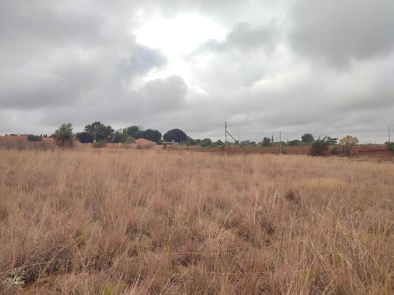 A view of a vacant residential plot covered in dry grass, offering a blank canvas for future development.