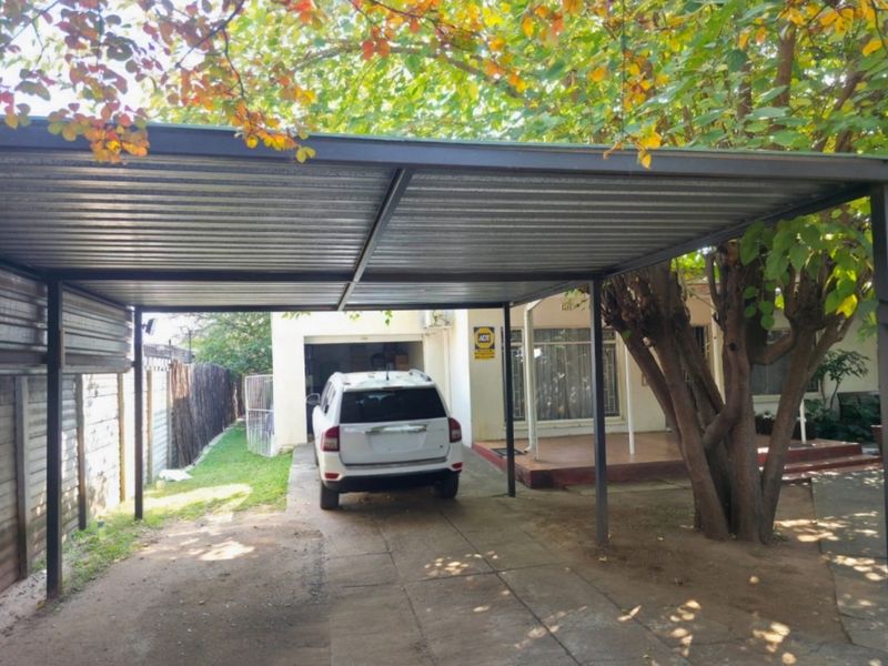 Front exterior view featuring a metal carport structure over a paved driveway, leading to the main house entrance and patio area.