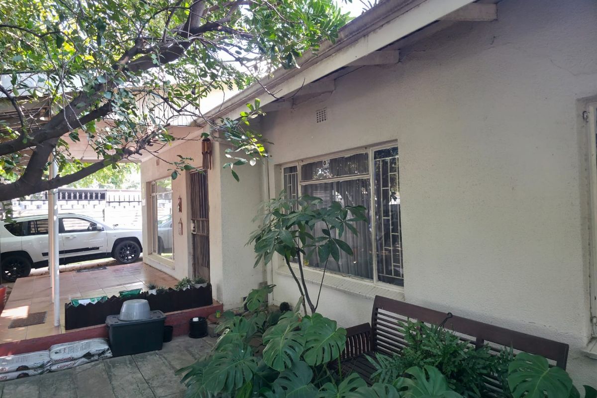 Rear exterior view of the house featuring a paved patio area, security bars on windows, and a covered walkway.
