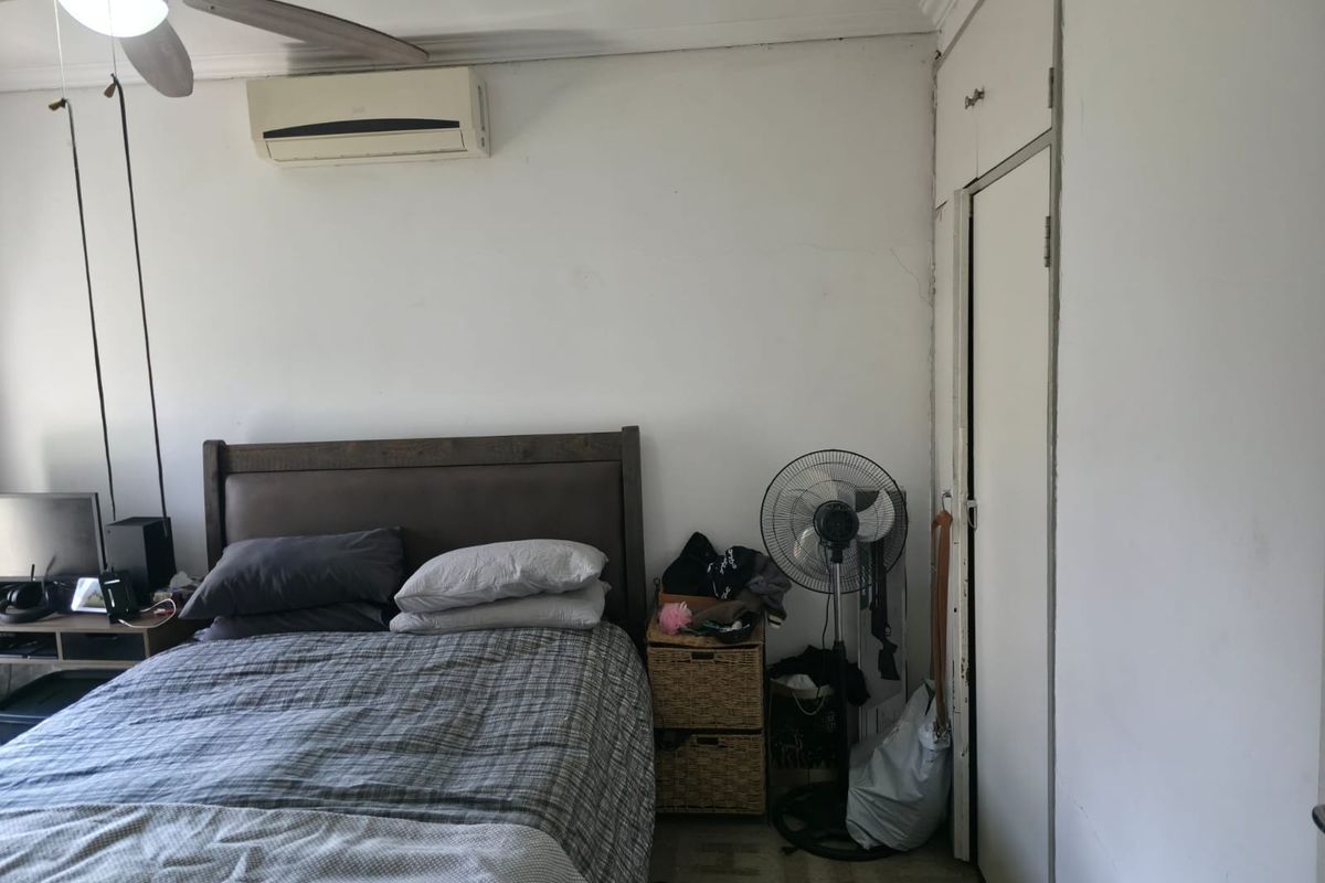 A bedroom featuring a ceiling fan, split-system air conditioning, and built-in storage, showing signs of wear on the walls and door frames.