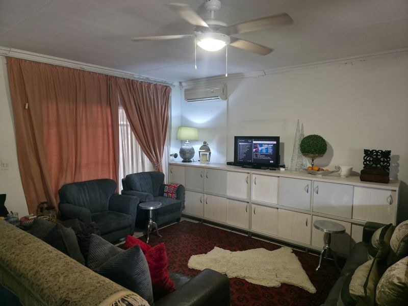 A comfortable living room featuring built-in storage cabinetry, a ceiling fan, and a wall-mounted air conditioning unit.