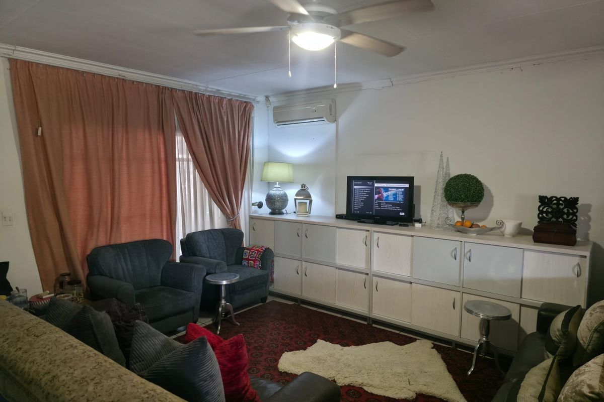 A comfortable living room featuring built-in storage cabinetry, a ceiling fan, and a wall-mounted air conditioning unit.