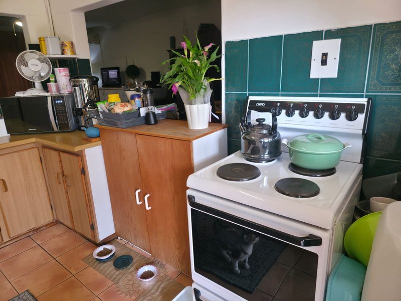 A functional kitchen area featuring a freestanding electric stove, tiled splashback, and traditional wooden cabinetry with tiled flooring.
