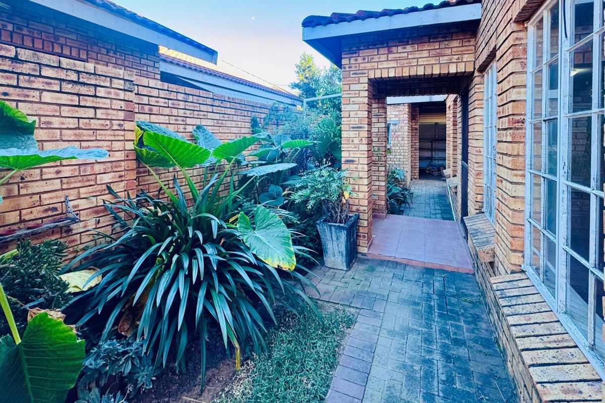 A side walkway featuring exposed brick walls, paved flooring, and established garden beds leading toward the rear of the property.