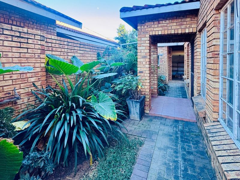 A side walkway featuring exposed brick walls, paved flooring, and established garden beds leading toward the rear of the property.