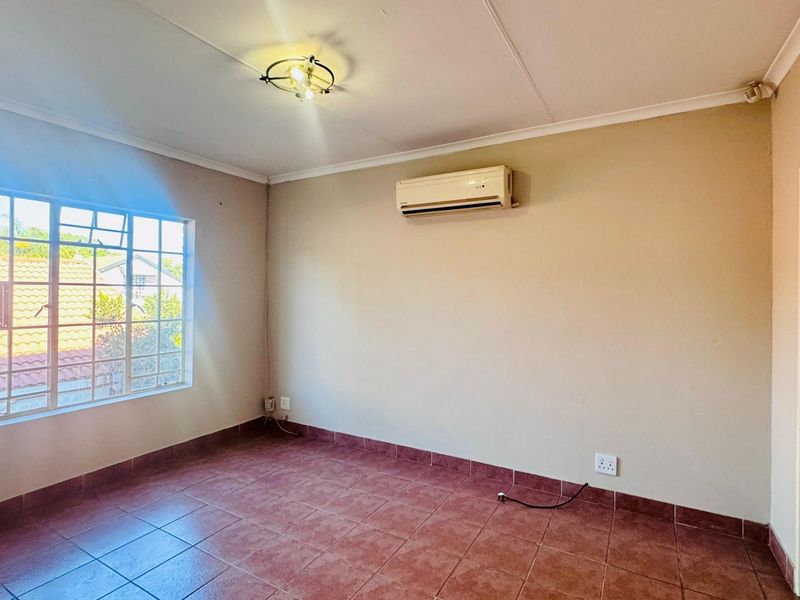 An empty bedroom featuring tiled flooring, a wall-mounted air conditioning unit, and natural light from a large window.