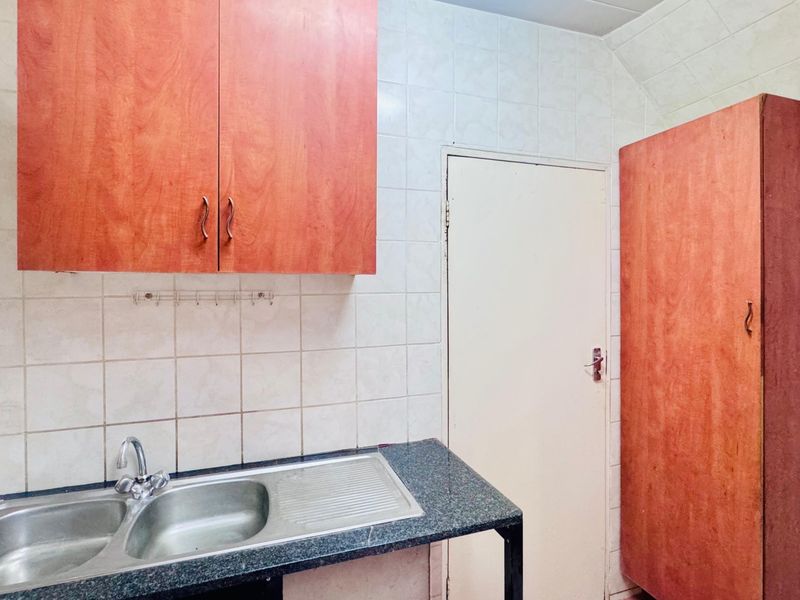 A functional kitchen area featuring a double bowl stainless steel sink, granite countertops, tiled splashbacks, and built-in wooden cabinetry.