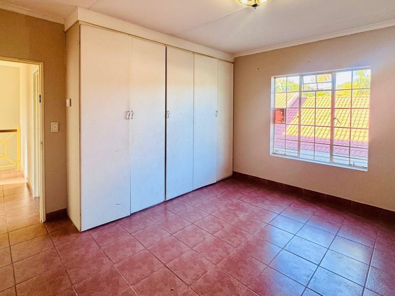 An empty bedroom featuring built-in cupboards, tiled flooring, and a steel-framed window, offering a blank canvas for renovation or interior design updates.