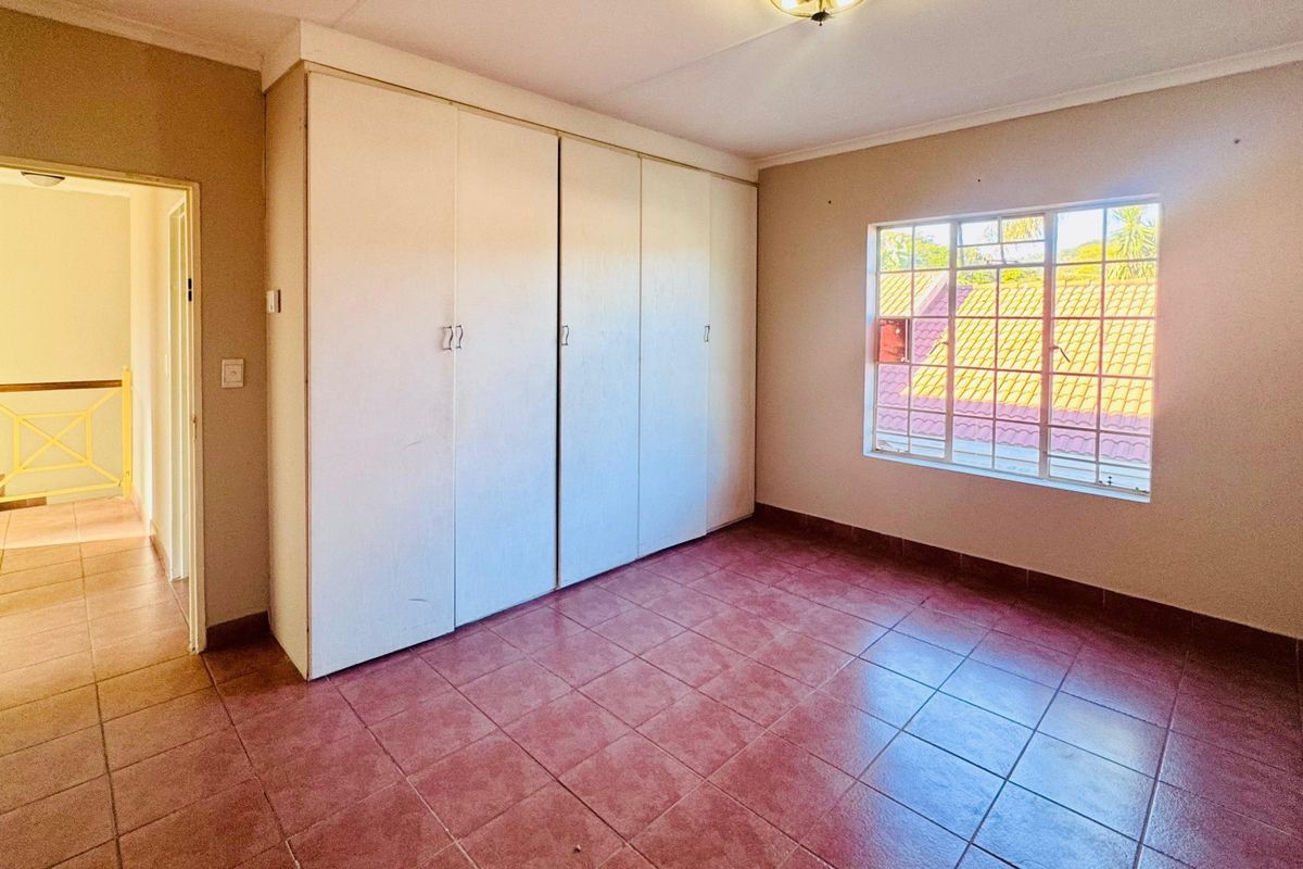 An empty bedroom featuring built-in cupboards, tiled flooring, and a steel-framed window, offering a blank canvas for renovation or interior design updates.