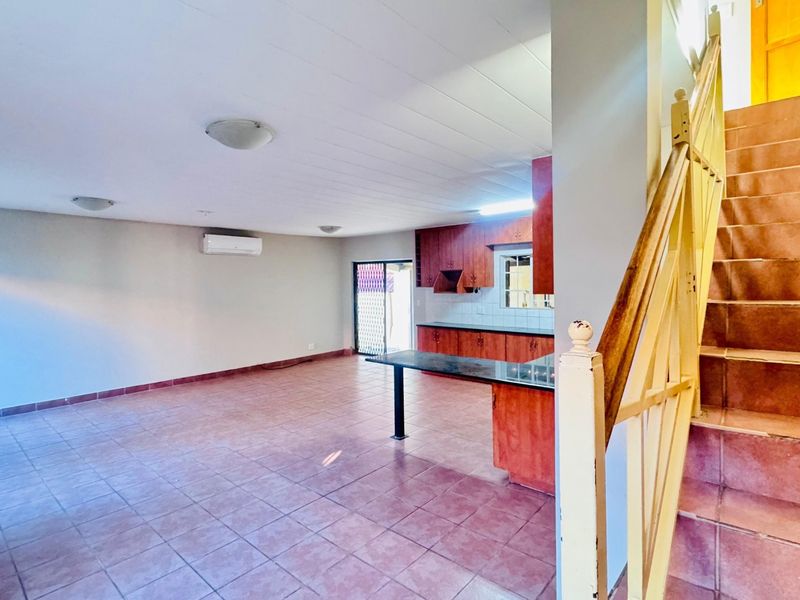 Open-plan living area featuring a kitchen with wooden cabinetry, a breakfast island, and a staircase leading to the upper level.