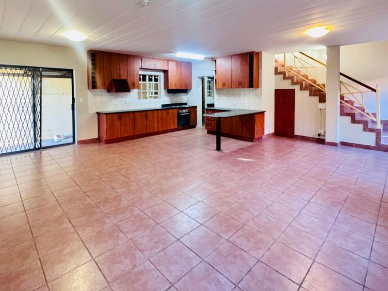 Spacious open-plan kitchen and living area featuring tiled floors, built-in wooden cabinetry, and a staircase leading to the upper level.