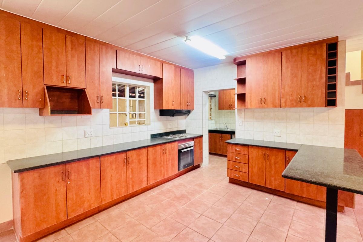 A spacious kitchen featuring extensive wooden cabinetry, granite countertops, a built-in oven and hob, and a breakfast bar, with a separate scullery area visible.