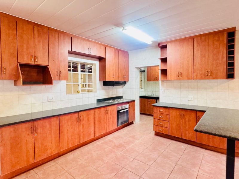 A spacious kitchen featuring extensive wooden cabinetry, granite countertops, a built-in oven and hob, and a breakfast bar, with a separate scullery area visible.