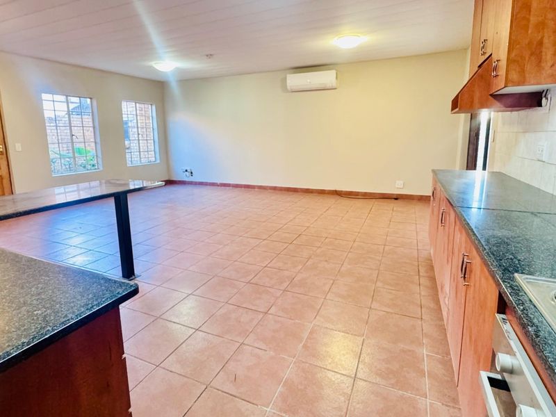 Spacious open-plan living and kitchen area featuring tiled floors, built-in cabinetry with granite countertops, and a wall-mounted air conditioning unit.