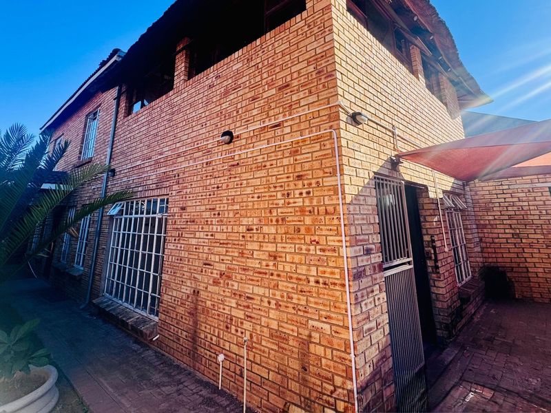 Rear exterior view of a face brick house featuring a paved patio area with a shade sail and security bars on windows.