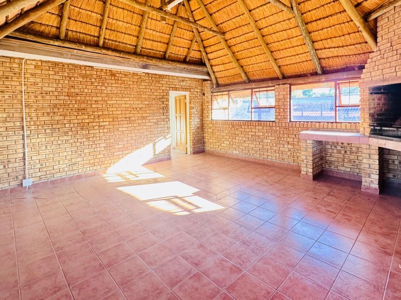 Spacious enclosed patio featuring a traditional thatched roof, exposed brick walls, tiled flooring, and a built-in braai area, perfect for outdoor entertaining.