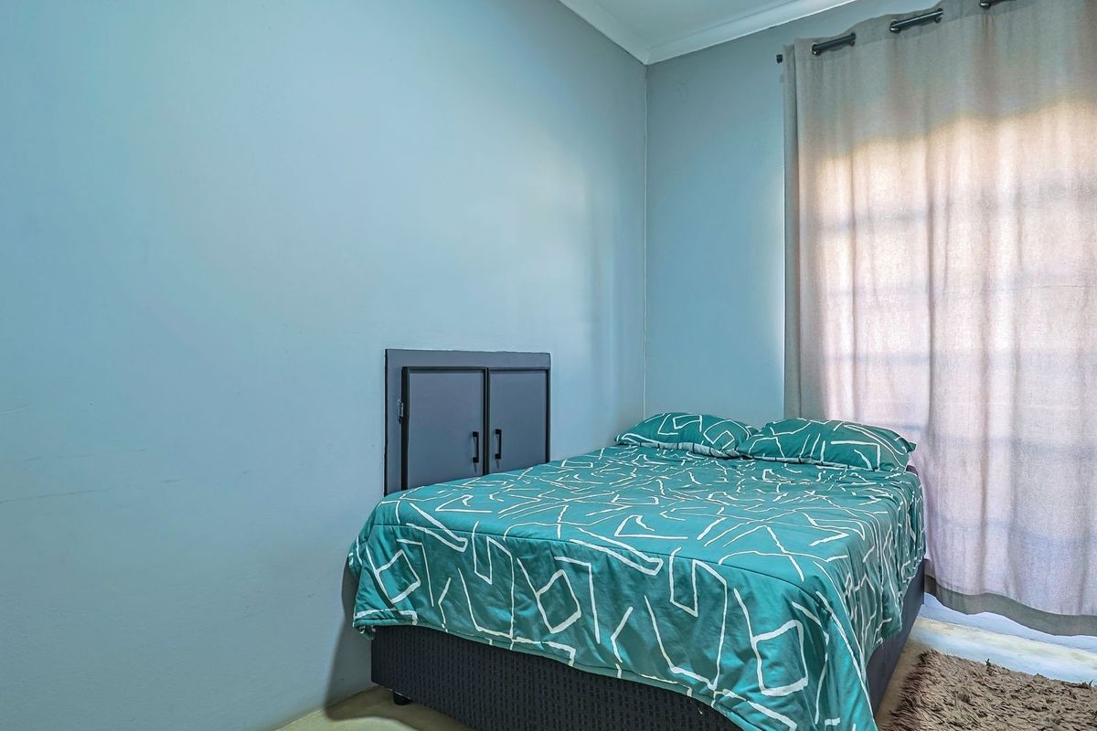 A functional bedroom featuring a built-in wall cupboard and natural light provided by a window with curtain rails.