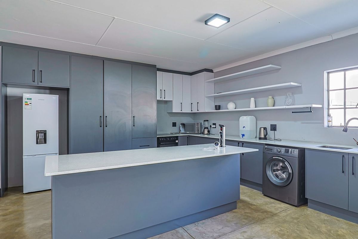 Modern kitchen featuring grey cabinetry, a central island with stone countertops, floating shelving, and integrated laundry appliances.