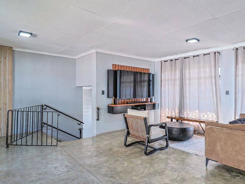 Spacious living room featuring polished concrete floors, a modern built-in media console, and a striking wood panel feature wall with staircase access.