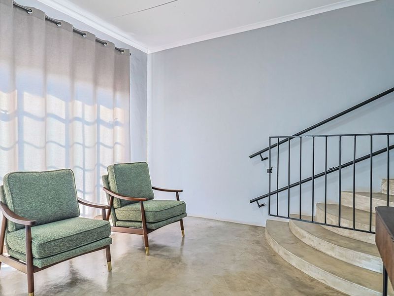 A bright living area featuring polished concrete floors, a curved staircase with a modern metal handrail, and large windows with soft curtains.