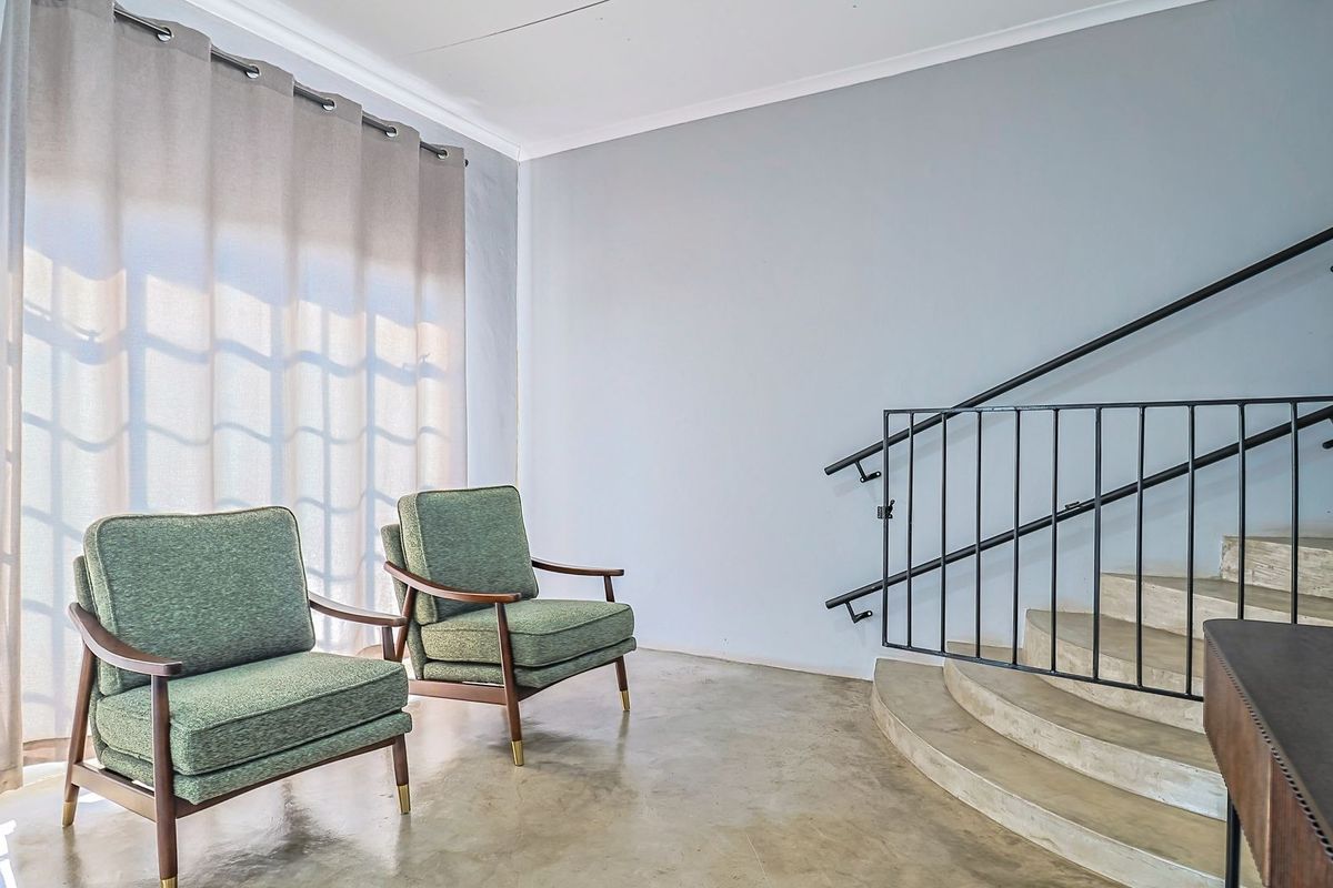 A bright living area featuring polished concrete floors, a curved staircase with a modern metal handrail, and large windows with soft curtains.