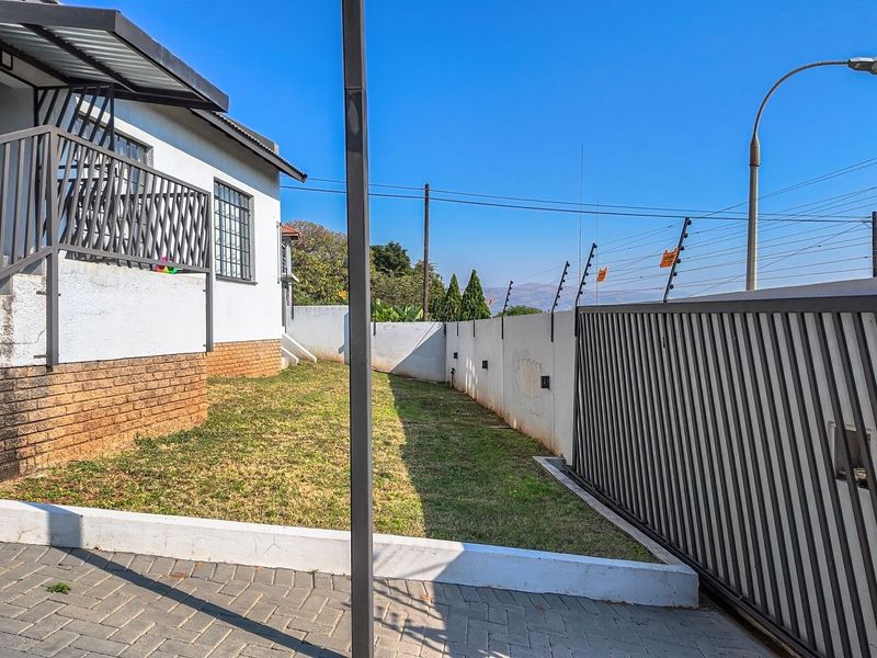 Front exterior view featuring a paved driveway, sliding gate, electric fencing, and a small lawn area with a brick retaining wall.