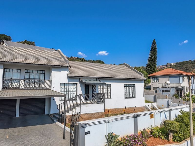 Front elevation of a double-story residential property featuring a paved driveway, double garage, balcony, and secure perimeter wall with electric fencing.