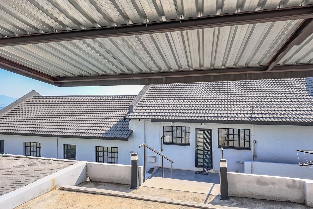 A rear exterior view featuring a covered patio area, concrete stairs with metal handrails, and a multi-pitched tiled roof structure.