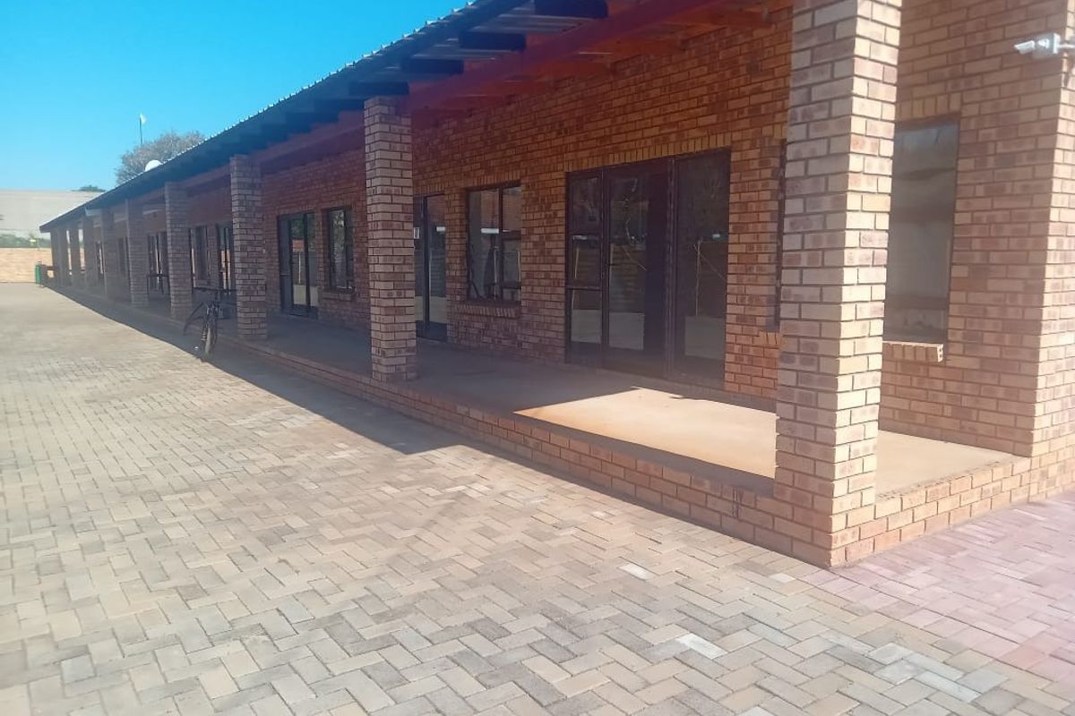 A long covered veranda featuring exposed brick pillars and paved flooring, providing access to the apartment through multiple glass sliding doors.