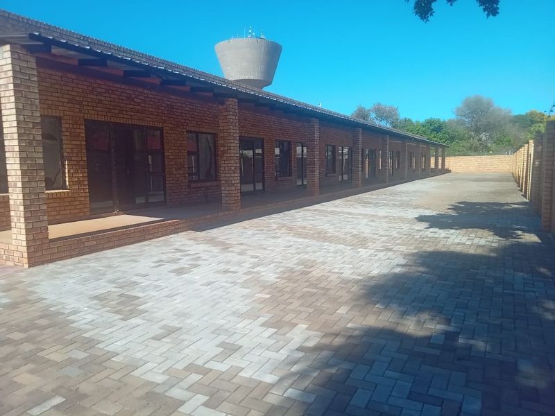 A spacious exterior rear courtyard featuring durable face brick construction, a covered walkway with brick pillars, and extensive paved ground surfaces.