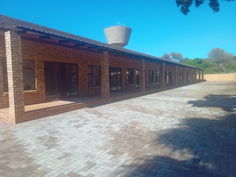 A spacious exterior rear courtyard featuring a long face brick building with a covered walkway, paved flooring, and multiple sliding glass door access points.