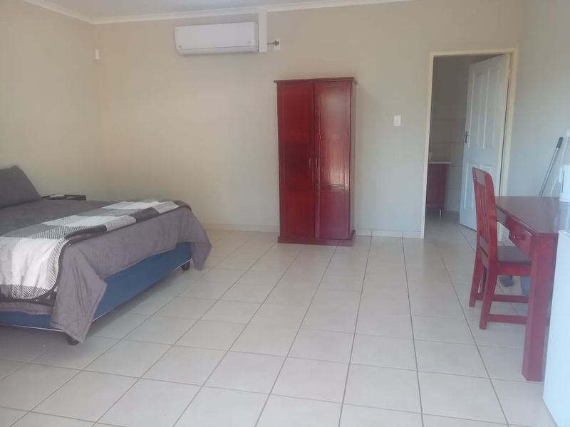 A spacious bedroom featuring neutral walls, tiled flooring, and a wall-mounted split-system air conditioner, with direct access to an adjoining room.