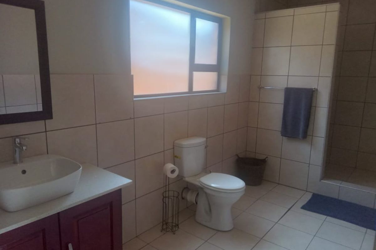 A functional bathroom featuring a vessel sink vanity, a standard toilet, and a walk-in shower with neutral wall and floor tiling.
