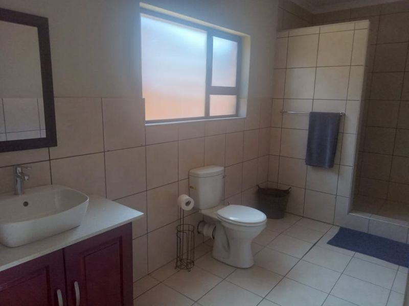 A functional bathroom featuring a vessel sink vanity, a standard toilet, and a walk-in shower with neutral wall and floor tiling.