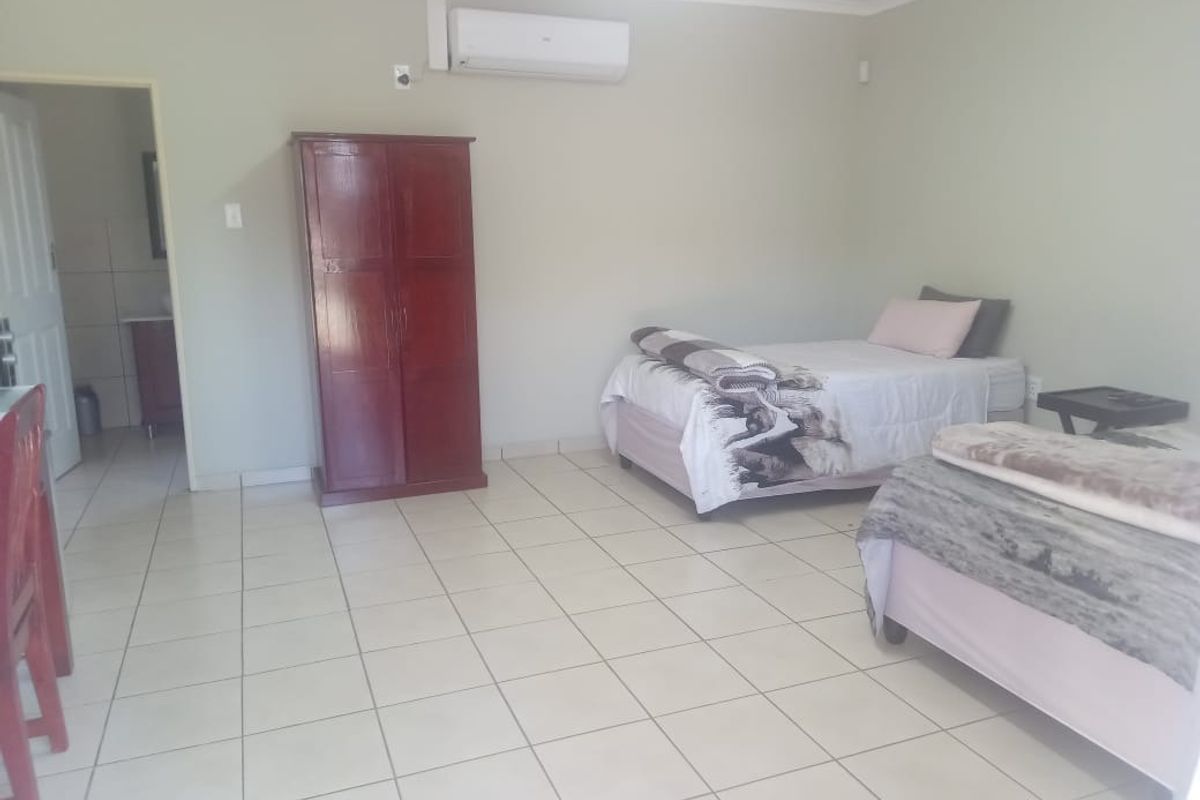 A spacious bedroom featuring tiled flooring, neutral wall tones, and a wall-mounted air conditioning unit, with an adjoining en-suite bathroom.