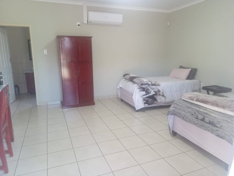 A spacious bedroom featuring tiled flooring, neutral wall tones, and a wall-mounted air conditioning unit, with an adjoining en-suite bathroom.