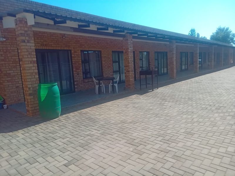 A long covered patio area featuring brick construction, paved flooring, and multiple sliding glass door access points to the apartment units.