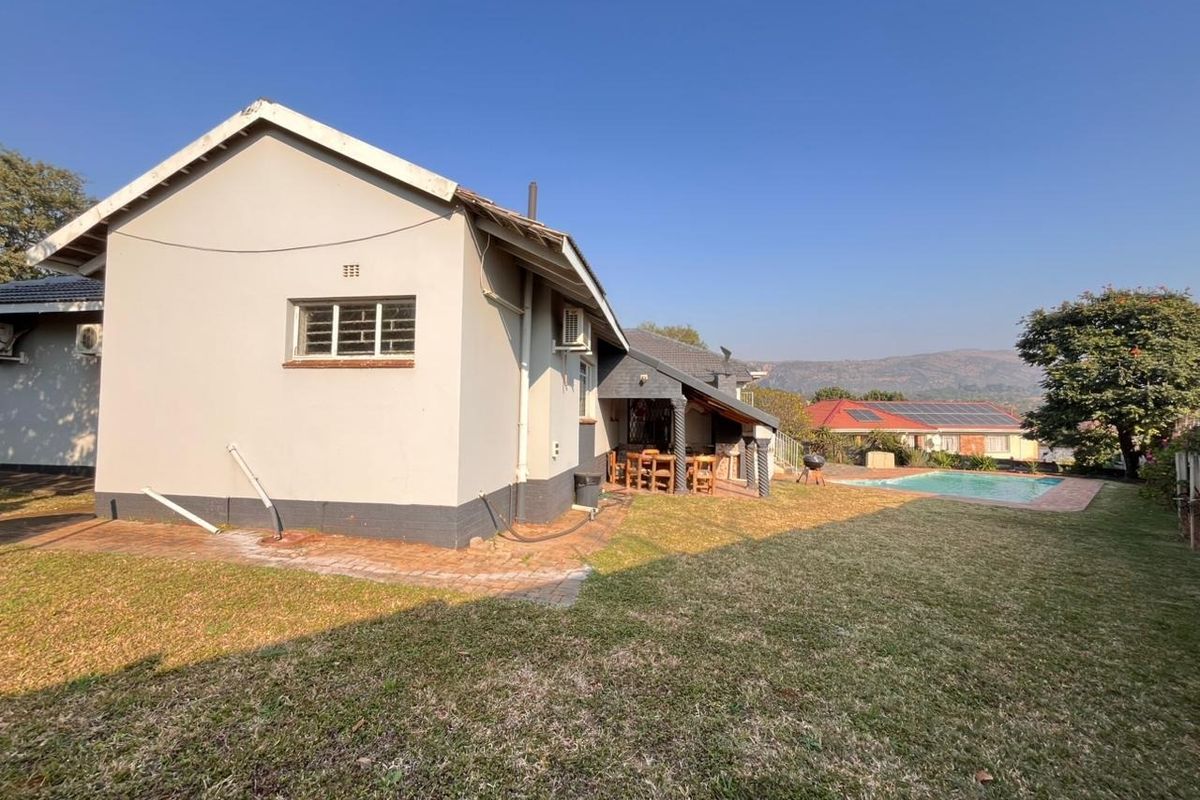 Rear view of the property featuring a swimming pool, landscaped garden, and a covered patio area with brick paving.