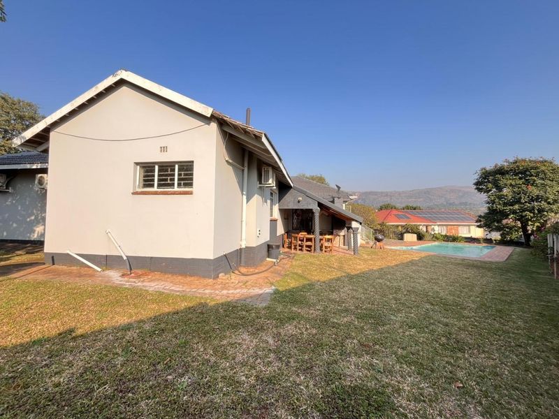 Rear view of the property featuring a swimming pool, landscaped garden, and a covered patio area with brick paving.