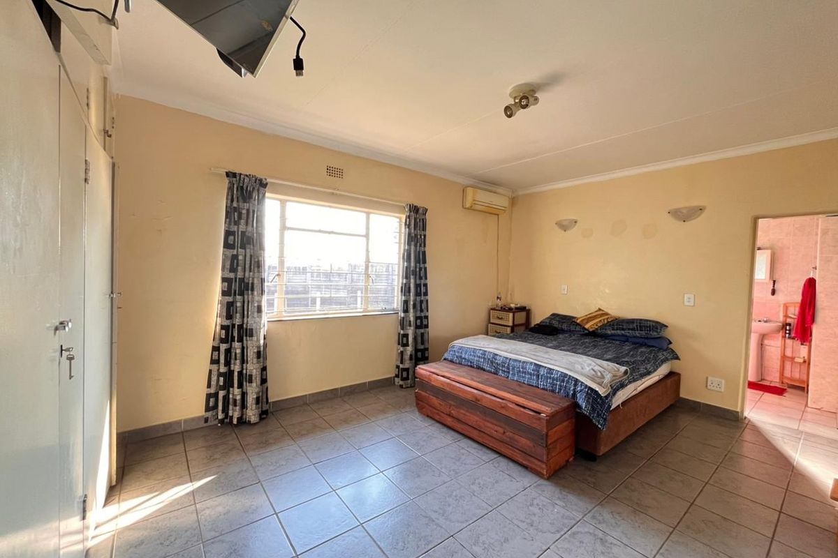 Spacious bedroom featuring tiled flooring, built-in cupboards, and a wall-mounted air conditioning unit, with direct access to an en-suite bathroom.